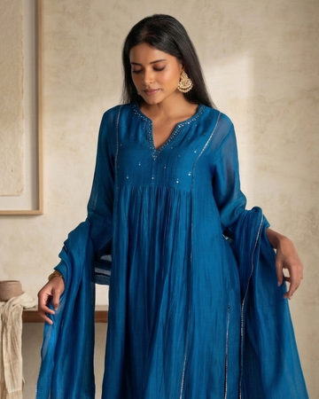 Woman in a blue traditional outfit standing in a room with a neutral color scheme.
