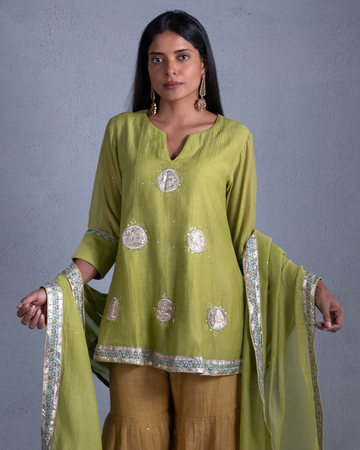 Woman wearing a green and beige traditional outfit with a plain background